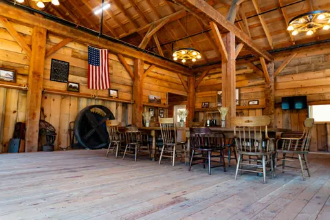 An interior view of a rustic wooden barn with a long table and chairs.