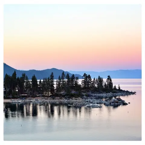 A calm lake reflecting trees and a colorful twilight sky.