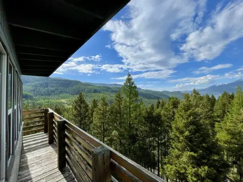 A view of forested mountains and a cloudy blue sky from a wooden balcony.