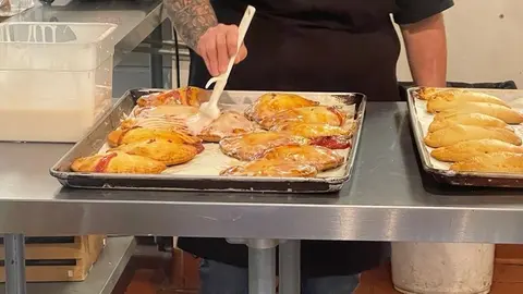 A person glazes pastries on a baking sheet in a kitchen.