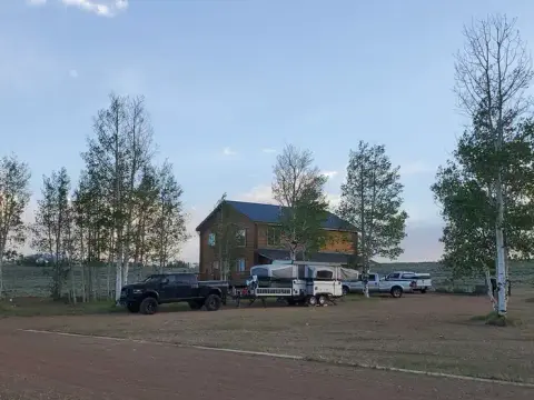 A large wooden cabin surrounded by trees with parked trucks and a pop-up camper trailer.