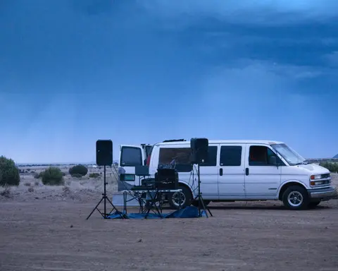 A white van parked in an arid landscape with audio equipment set up beside it.