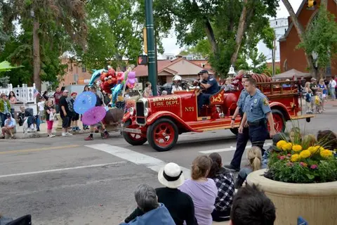 An antique fire truck participates in a parade while crowds watch from the street.