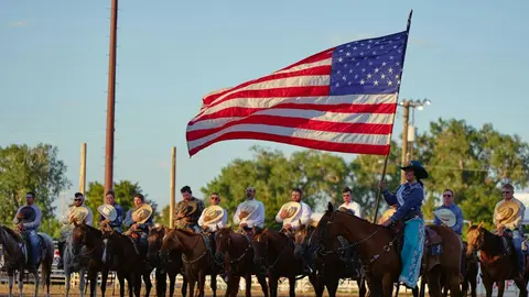 A line of people on horseback, with one person holding a large American flag.