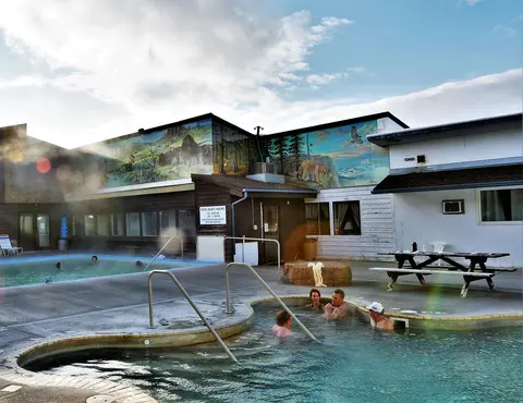 People enjoy soaking in an outdoor hot spring pool next to a building with murals.