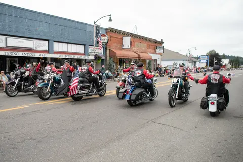 A group of motorcyclists ride down a street lined with buildings and spectators.