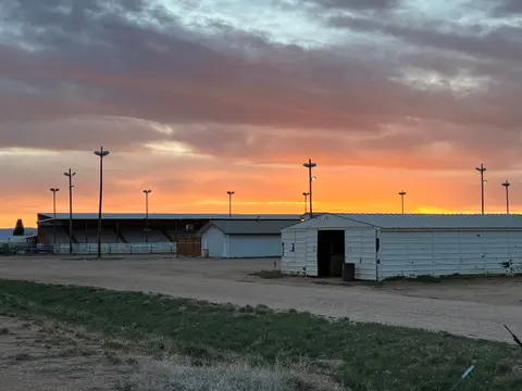 A vibrant sunset over an outdoor arena and outbuildings.