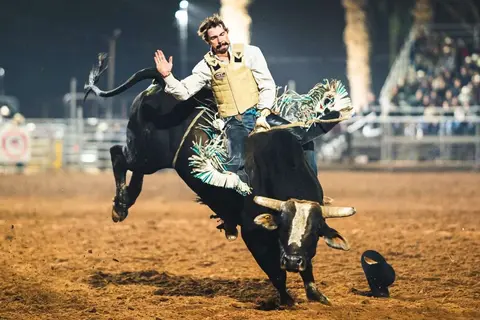 A cowboy riding a bucking bull in an arena.