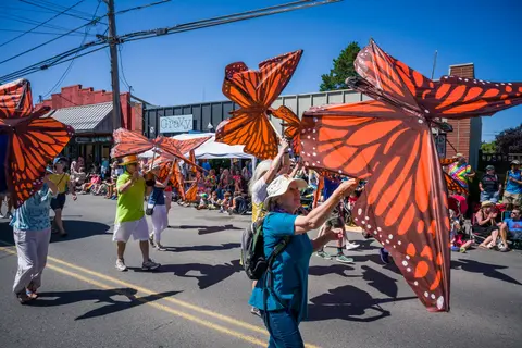 People walk in a street parade carrying large butterfly props.