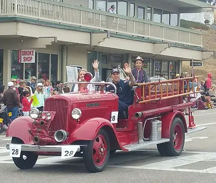 A vintage fire truck carrying people waving during a parade.
