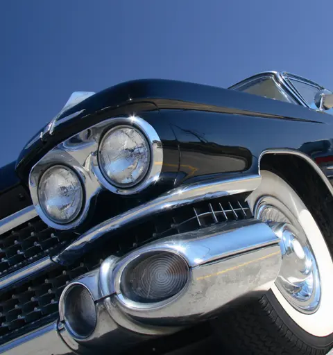 A close-up low-angle view of the front of a classic black car with chrome detailing and white-wall tires.