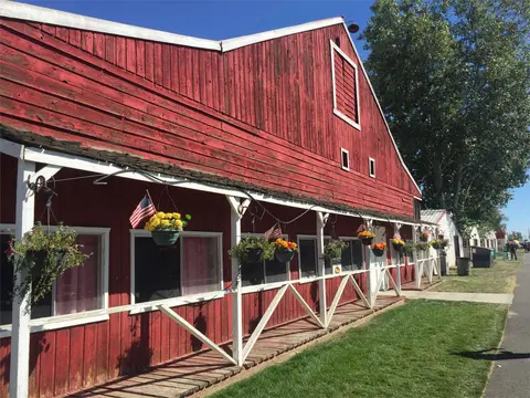 A red wooden barn with a covered porch decorated with hanging flower baskets and small American flags.