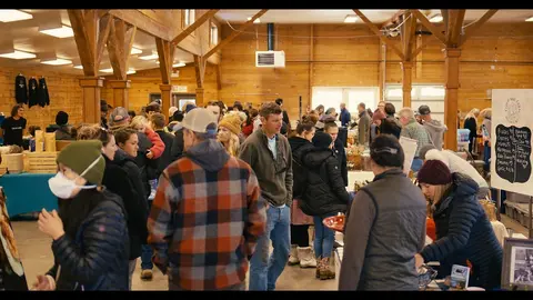 People gather and shop inside a large wooden building.