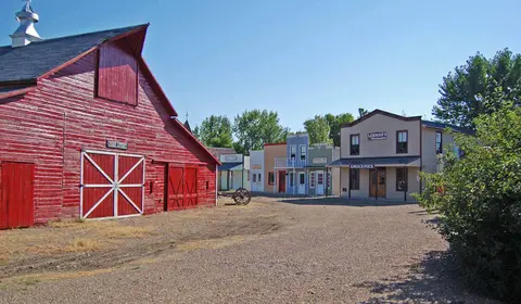 An outdoor view of a historical village with a large red barn and old-fashioned storefronts.