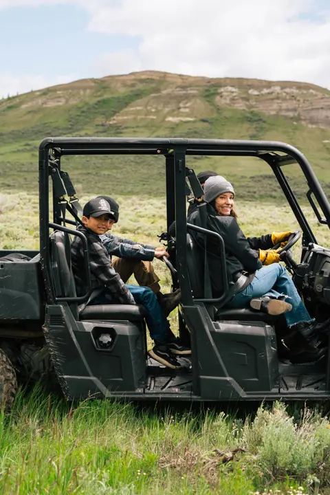 A woman and children ride in an all-terrain vehicle through a landscape.