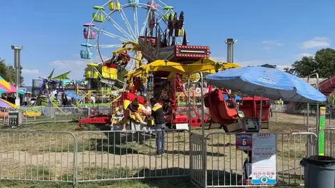 Carnival rides are set up outdoors with a ferris wheel in the background.