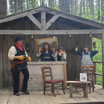 People in period costumes perform an outdoor play on a wooden stage.