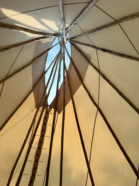 Looking up from inside a tipi at the wooden poles and opening at the top.