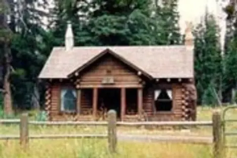 A rustic log cabin sits in a clearing surrounded by trees.