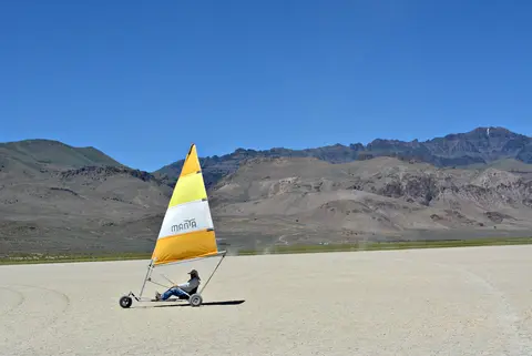 A person rides a land sail vehicle across a dry lake bed with mountains in the background.