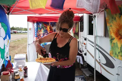 A woman pours syrup onto a funnel cake at an outdoor food stand.
