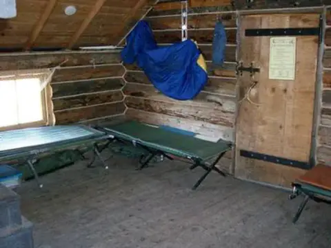 Interior of a rustic log cabin with cots and a wooden door.
