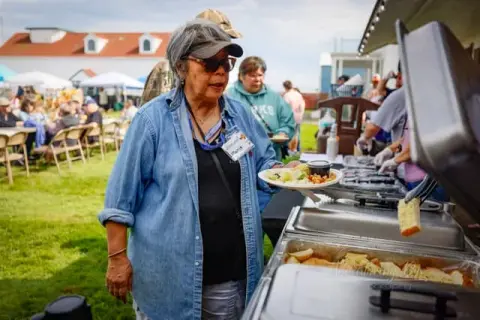 A woman holds a plate of food at an outdoor buffet line.