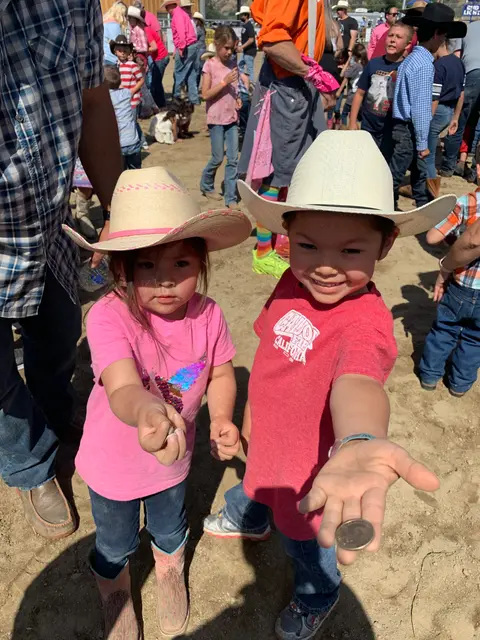 Two children wearing cowboy hats show coins in their hands at an outdoor event.