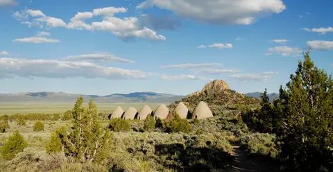 A row of stone kilns sits in a desert landscape under a blue sky with clouds.