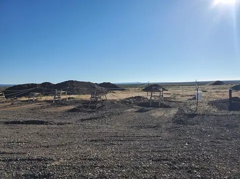 An outdoor mining or excavation site with piles of dirt under a bright blue sky.