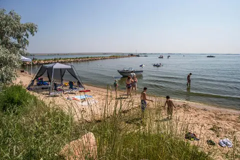 People enjoy a sunny day at a sandy beach by a large body of water.