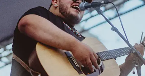 A man plays an acoustic guitar and sings into a microphone.