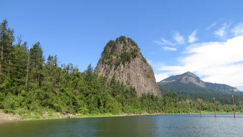 A large rock formation rises above a forested shoreline and a river.
