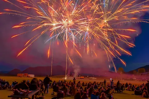 A crowd watches a large fireworks display over a field at night.