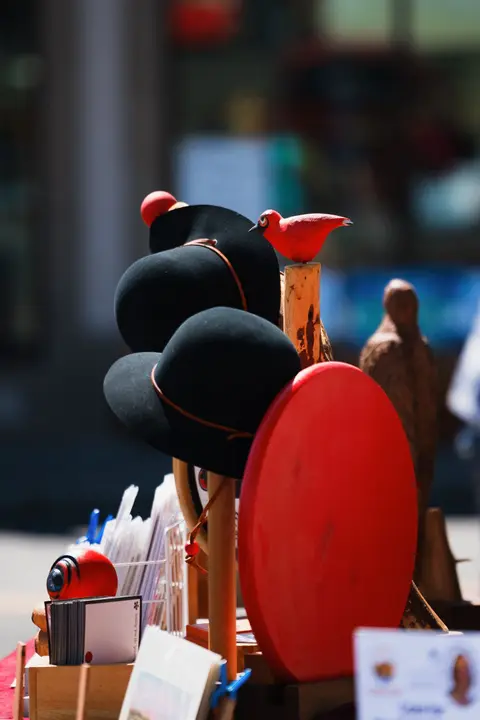 A close-up view of black hats and red wooden crafts on display outdoors.