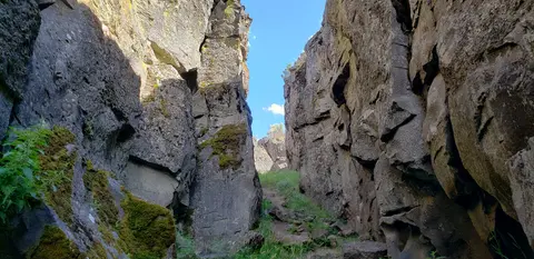 A narrow path between tall rocky cliffs under a blue sky.