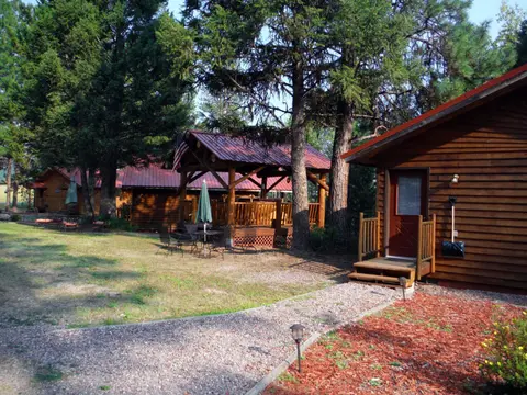 Wooden cabins and a gazebo surrounded by trees and a grassy yard.