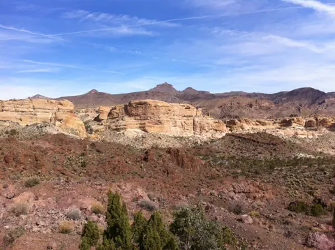 A desert landscape featuring red rock formations and distant mountains under a blue sky.