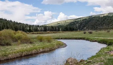 A winding stream flows through a grassy valley beneath a cloudy sky.