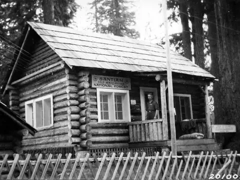 A historic black and white photo of a log cabin with a sign for Santiam National Forest field headquarters.