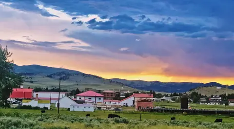 A sunset over a rural valley with hills and buildings.