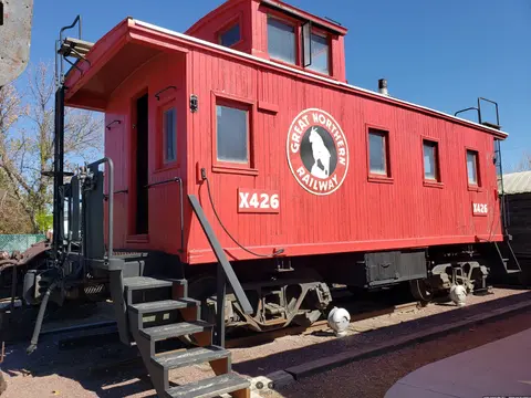 A red caboose sits on railroad tracks outdoors.