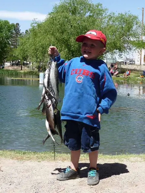A young boy proudly displays a stringer of fish by a pond.