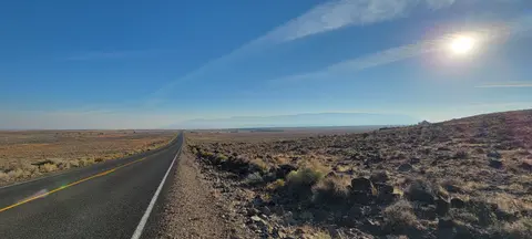 A long straight road stretching across a desert landscape under a sunny blue sky.