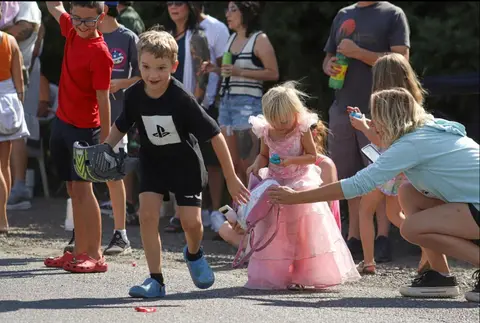 Children participate in an outdoor event with adults watching.