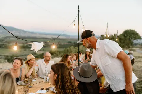 People dining outdoors at a long table with string lights.