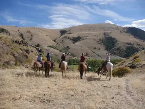 Five people on horseback pointing towards hills.