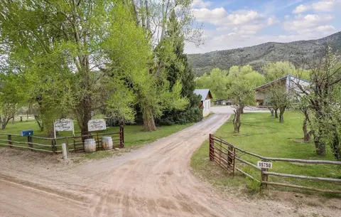 An exterior view of a rural property with a dirt driveway and buildings surrounded by trees and mountains.