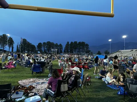 A large crowd of people gathered on a grassy field at dusk.