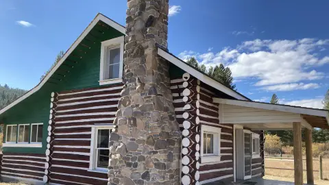 An exterior view of a log cabin with a stone chimney under a blue sky.